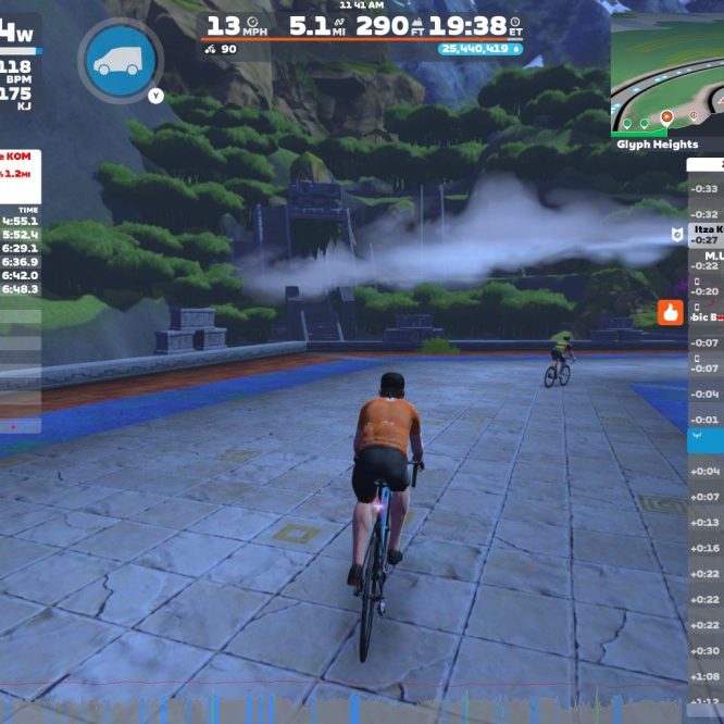 A cyclist wearing an orange jersey rides on a virtual road in a mountainous landscape, with a scoreboard displaying performance stats, nearby cyclists, and recent achievements. The scene includes lush greenery and a water feature in the background.