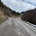 A winding dirt road surrounded by rocky terrain and sparse vegetation, with patches of snow visible on the ground. The scene is set under a cloudy sky, showcasing the mountainous landscape of Logan, Utah.