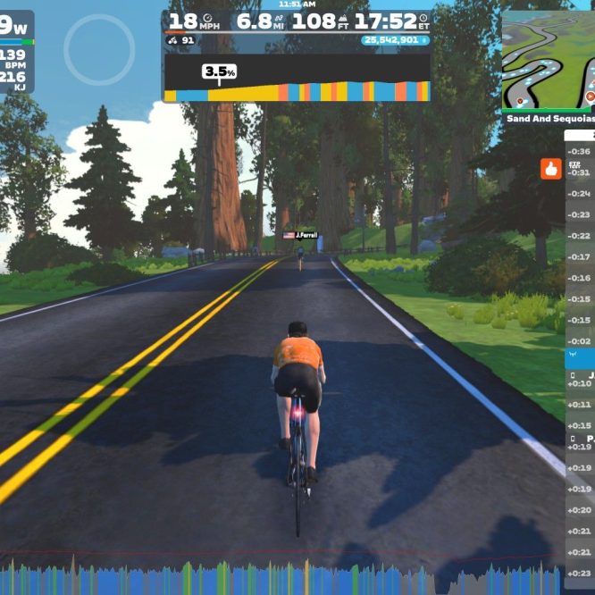 A cyclist wearing an orange shirt rides on a virtual road surrounded by trees in the Zwift app. The display shows various stats, including power output, speed, and distance traveled, along with a leaderboard of nearby riders. The scene captures a scenic, digital landscape intended for cycling workouts.