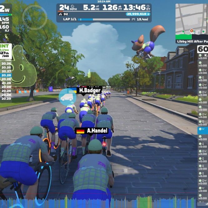 A group of cyclists riding together on a virtual street in Zwift, featuring colorful avatars with a leaderboard displaying their rankings and stats. The scene includes trees lining the street and a large animated character in the background, set against a blue sky. The cyclists are wearing matching gear with the Zwift logo.