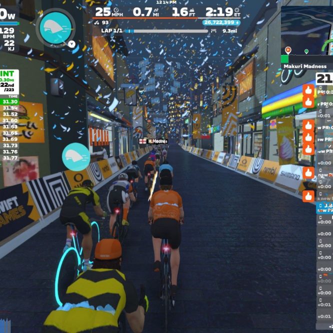 A virtual cycling race on Zwift, showing multiple cyclists in a colorful, animated cityscape with festive confetti. The scene includes on-screen data such as power output, speed, and rankings, with various cyclists riding closely together. The race is taking place on a flat course, indicated by the layout in the background.