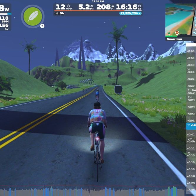 A cyclist is riding on a virtual road in Zwift, surrounded by green hills and mountains. The screen displays speed, power output, and other performance metrics. Nearby cyclists are listed on the right side. The setting is colorful with a clear blue sky and palm trees, indicative of a scenic environment.