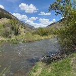 A scenic view of a river winding through lush greenery in Paradise, Utah, with mountains in the background and a partly cloudy sky.