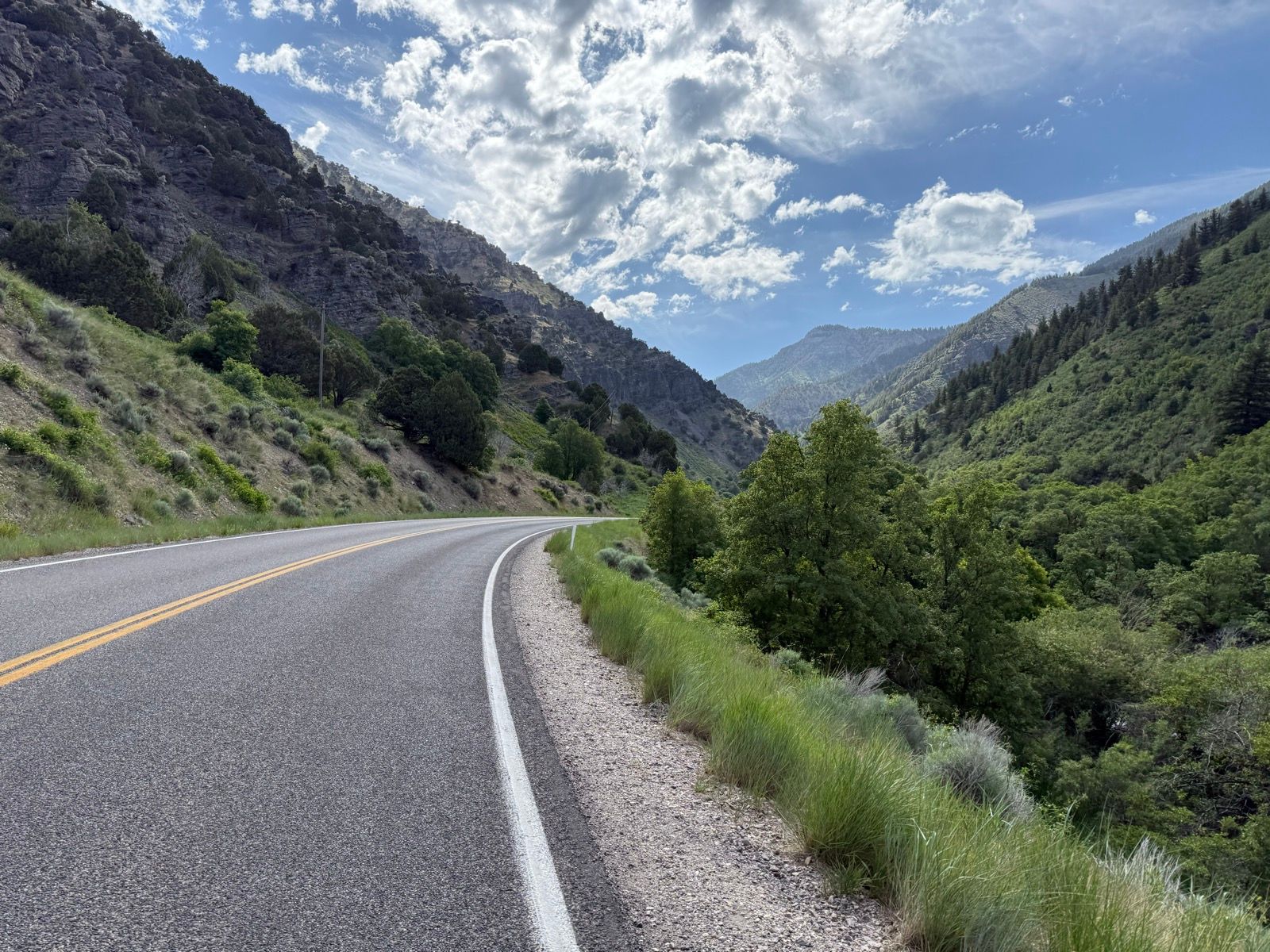 A winding road through a mountainous landscape at Porcupine Dam, Utah, surrounded by green hills and rocky cliffs under a partly cloudy sky.
