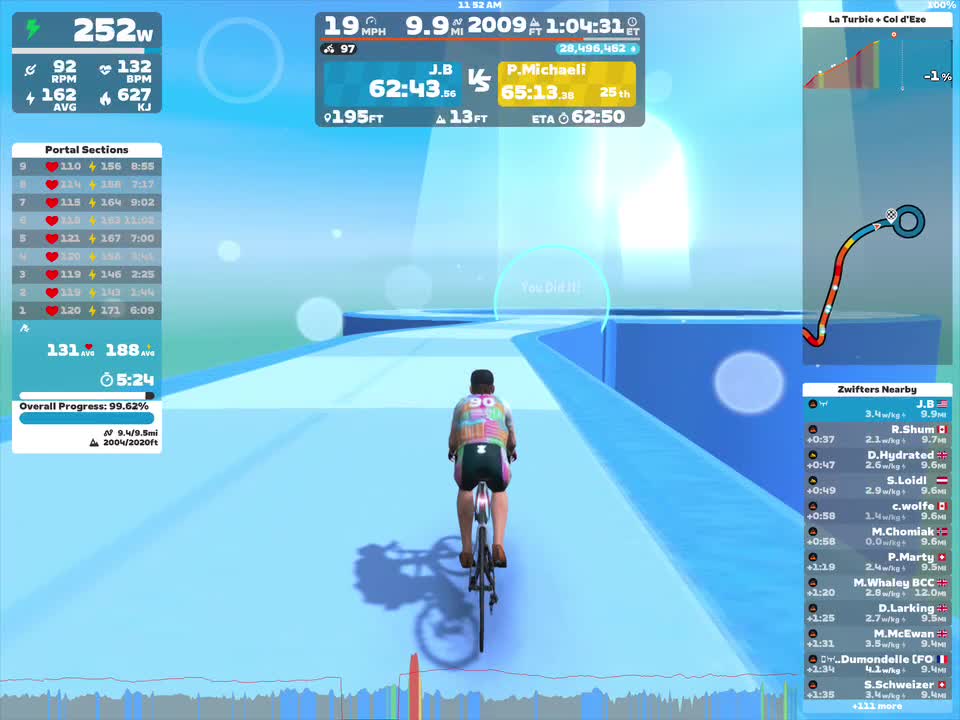 A cyclist in virtual gear rides on a digital blue track within the Zwift game. The display shows various performance metrics, including speed, power output, and distance covered, along with nearby competitors and progress information. A bright light source is visible in the background, creating a vibrant atmosphere.