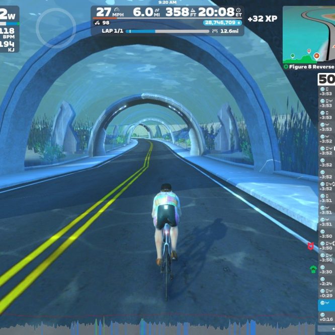 A cyclist rides on a virtual road in Zwift, surrounded by underwater-themed arches and aquatic plants. The screen displays cycling stats, including speed, distance, and power output, along with a leaderboard on the right side.