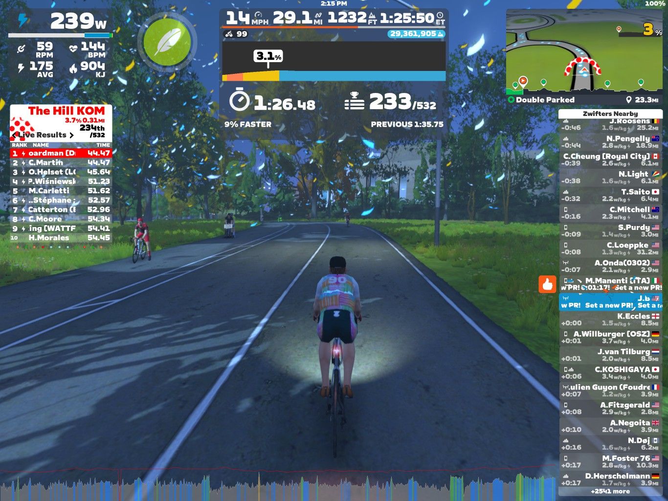 A cyclist rides on a virtual road in Zwift, surrounded by trees. The screen displays performance metrics, including power output (239 watts), speed (14 mph), and heart rate (144 bpm). A leaderboard shows ranking and times for various cyclists participating in the event, with a segment called