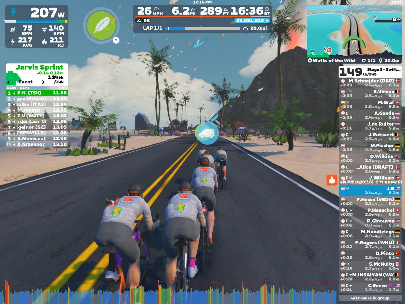 A group of cyclists riding on a virtual road in a scenic environment. The cyclists are close together, each wearing gray jerseys with the number 3 on the back. The background features palm trees, a sandy area, and a mountain, simulating a tropical landscape. The screen displays various performance statistics like speed, power, and heart rate, along with a leaderboard showing participant rankings.