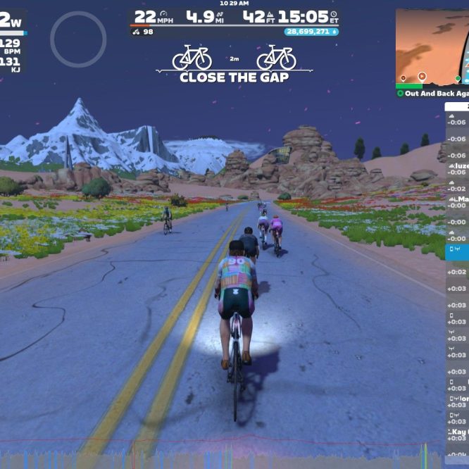 A group of virtual cyclists rides along a smooth, winding road surrounded by colorful flowers and grassy fields, with snow-capped mountains in the background. The scene is set in Zwift, featuring digital stats like speed, distance, and power output on the screen.