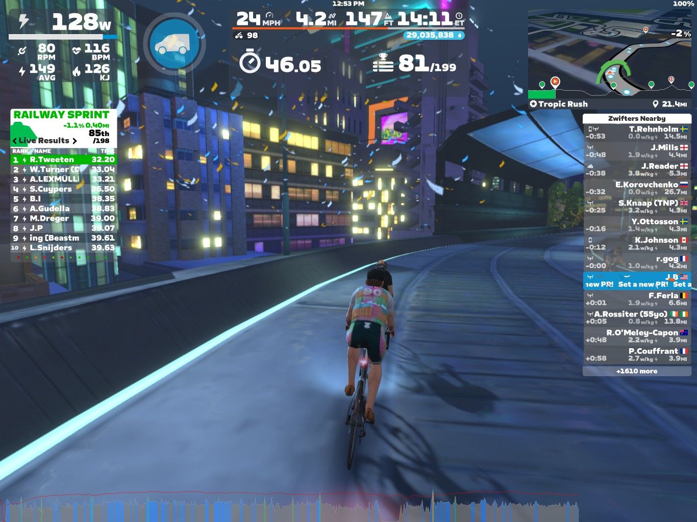 A cyclist is riding on a digital course in Zwift, surrounded by a colorful urban setting with buildings illuminated at night. The screen displays various statistics, including power output, speed, distance, and current rankings in a sprint event. In the background, there are graphics indicating nearby riders and their performance metrics.