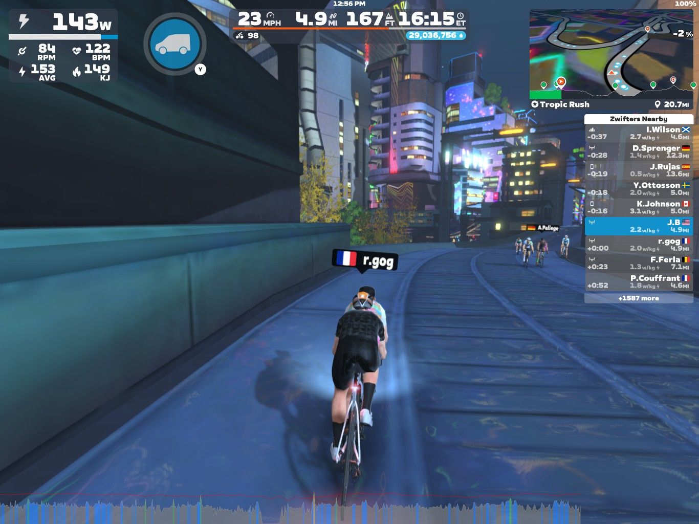 A cyclist is riding in a virtual environment on Zwift, navigating a futuristic cityscape with bright lights. The cyclist's current speed is 23 mph, with relevant stats displayed on-screen, including power output and distance. Nearby cyclists are listed in a sidebar, while a mini-map shows the course layout.