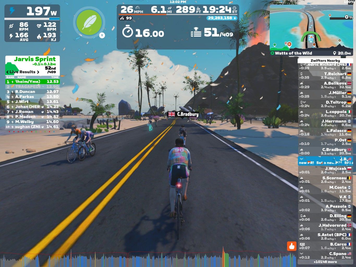 A digital cycling scene from Zwift, featuring riders on a virtual road under a colorful sky. The image includes performance stats such as speed, power output, and heart rate. Players are competing in the Jarvis Sprint event, with rankings and times displayed on the left side. Palm trees and a beach are visible in the background, enhancing the tropical atmosphere of the setting.