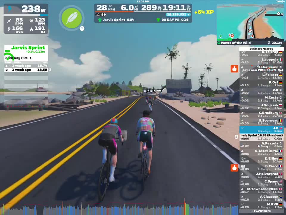 A digital cycling race in Zwift featuring several cyclists on a road surrounded by a beach landscape. The riders are competing in the