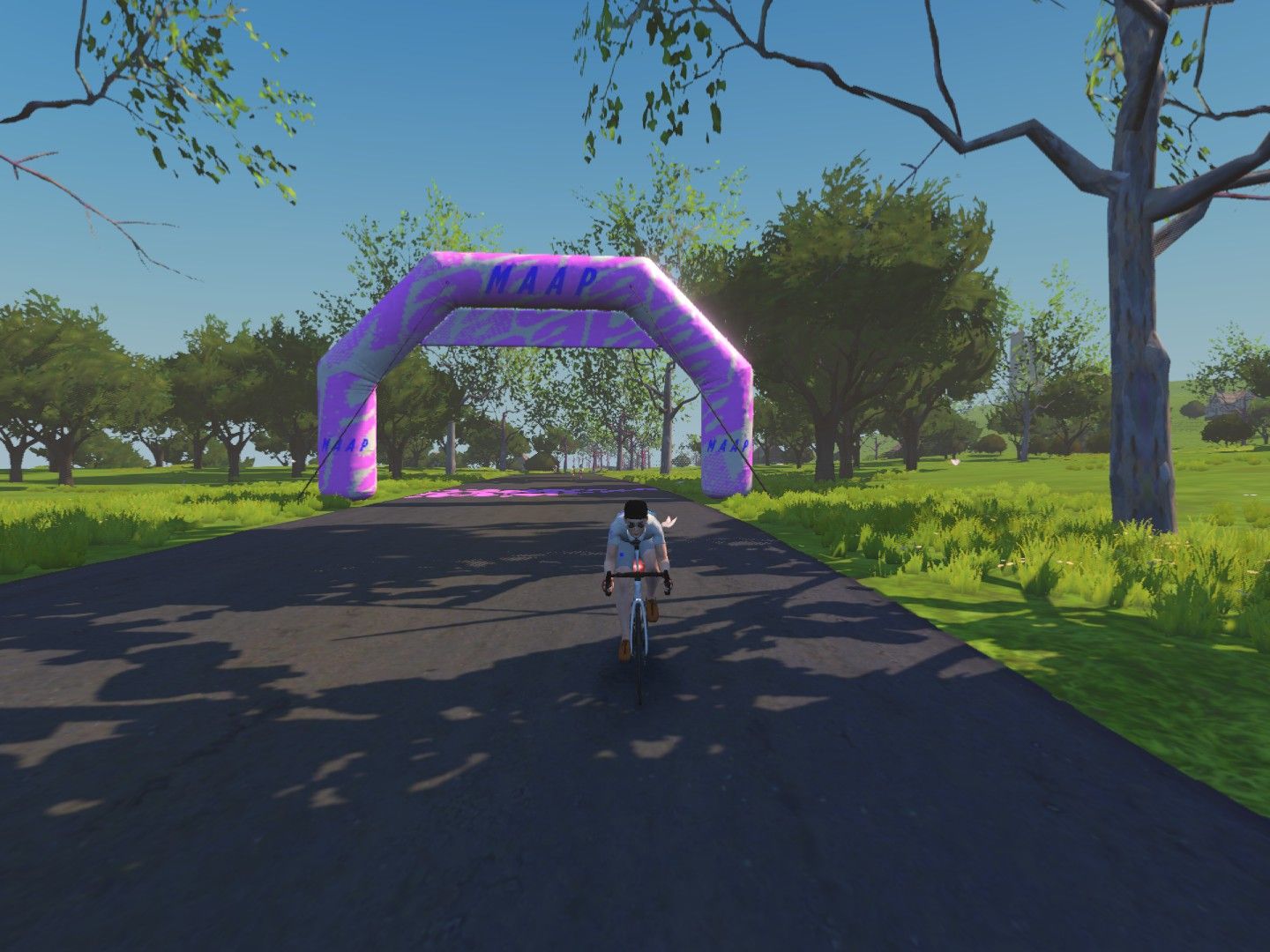 A cyclist in a white outfit rides under a purple inflatable arch that says 