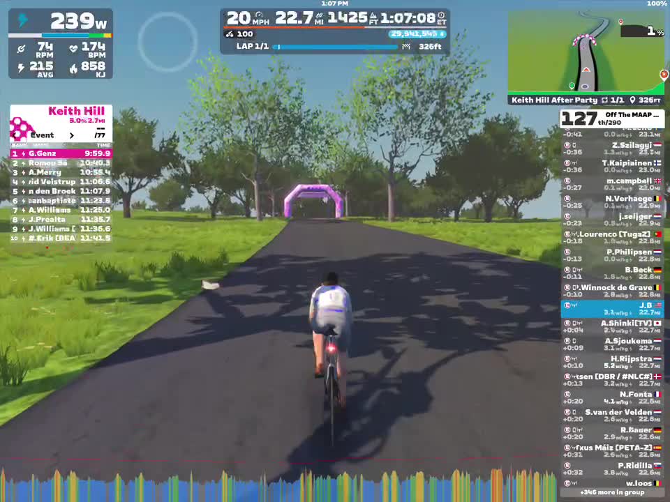 A cyclist is riding on a virtual road in the Zwift platform, with a purple arch in the distance. The scene includes green trees and a clear blue sky. The cyclist's speed and power data are displayed on the screen, along with race statistics and participant rankings.