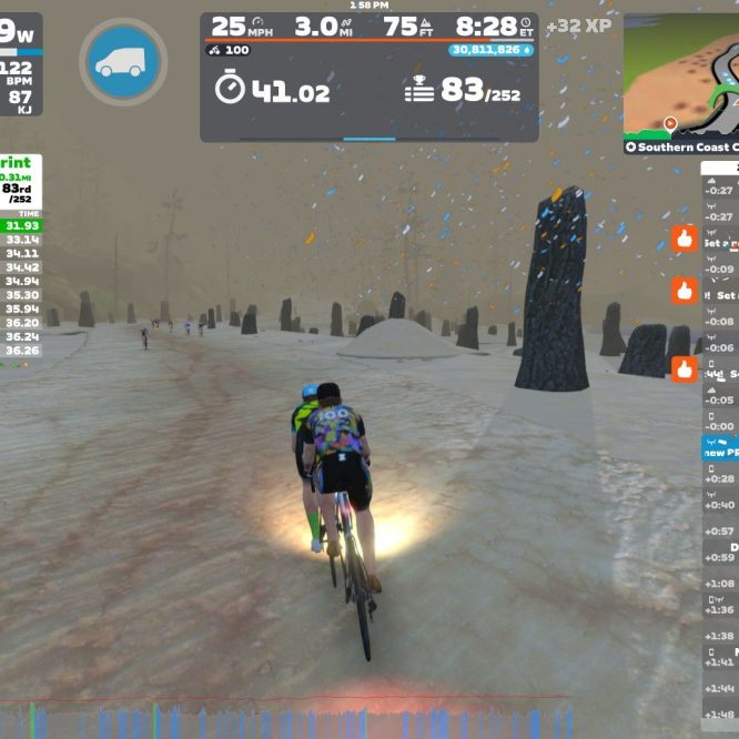 A cyclist participates in a virtual ride on Zwift, navigating a snowy landscape with large stone formations in the background. The screen displays live race results, performance metrics including speed and power output, and details of other nearby riders. The environment shows falling snow and a muted, foggy atmosphere.