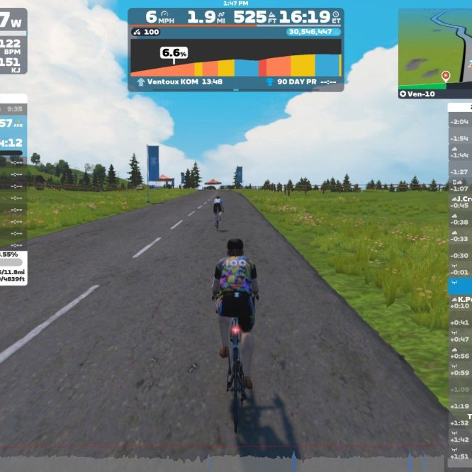 A cyclist rides on a virtual road in Zwift, with a rural landscape featuring grass and trees on either side. The screen displays various performance metrics, including speed, power output, and heart rate, as well as a leaderboard of other cyclists nearby. The weather appears clear with a blue sky and some clouds.