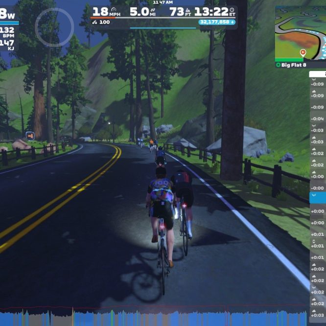 A group of cyclists riding on a virtual road in a scenic landscape, with tall trees and mountains in the background. The screen displays various statistics like power output, speed, and heart rate, along with a list of nearby cyclists.