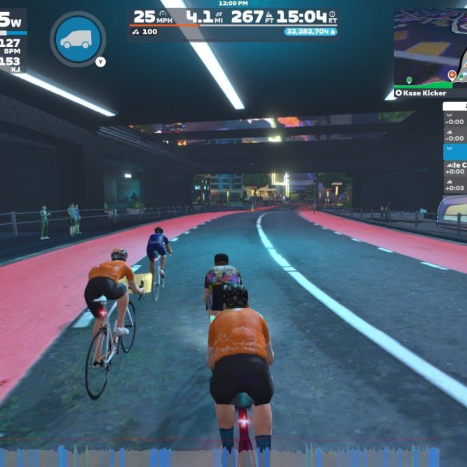 Alt text: A virtual cycling scene in Zwift showing four cyclists riding on a digital road. The background features a futuristic cityscape with spectators on the sidelines. There is a user interface displaying speed, power, and other cycling metrics.