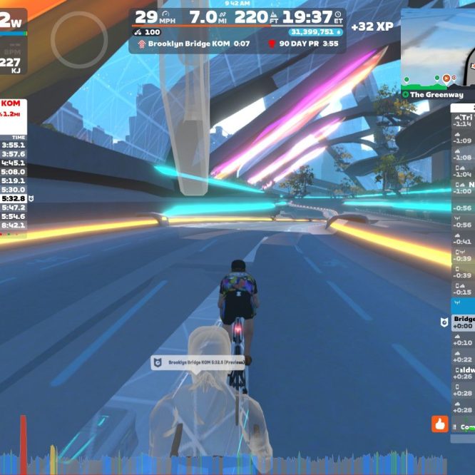 A cyclist is riding on a virtual path in Zwift, with information displayed on the screen. The stats show power output, speed, distance, and personal records for the Brooklyn Bridge segment. Colorful futuristic structures and trees are visible along the route. A mini-map in the corner displays the nearby area and other cyclists participating.