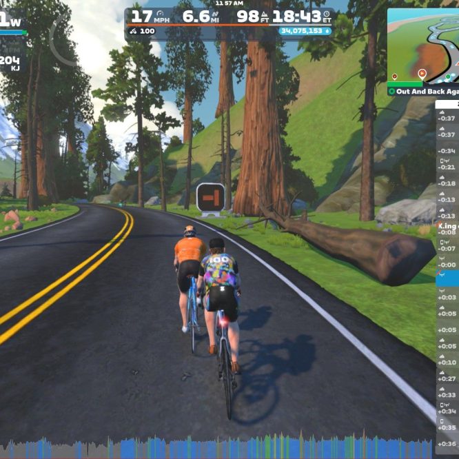 Two cyclists riding on a virtual road in Zwift's simulated environment, surrounded by trees and mountains. The screen displays their current speed, wattage, and other cycling stats, along with a mini-map and names of nearby riders.