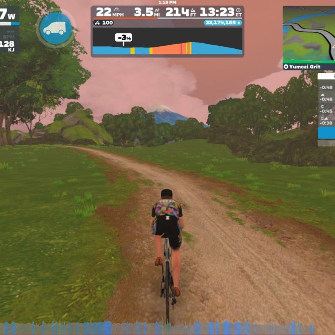 A cyclist rides on a dirt path in a virtual landscape, surrounded by trees and rolling hills. The display shows various cycling statistics, including speed, distance, and power output. The sky has a pinkish hue, indicating a dynamic environment in the Zwift platform.